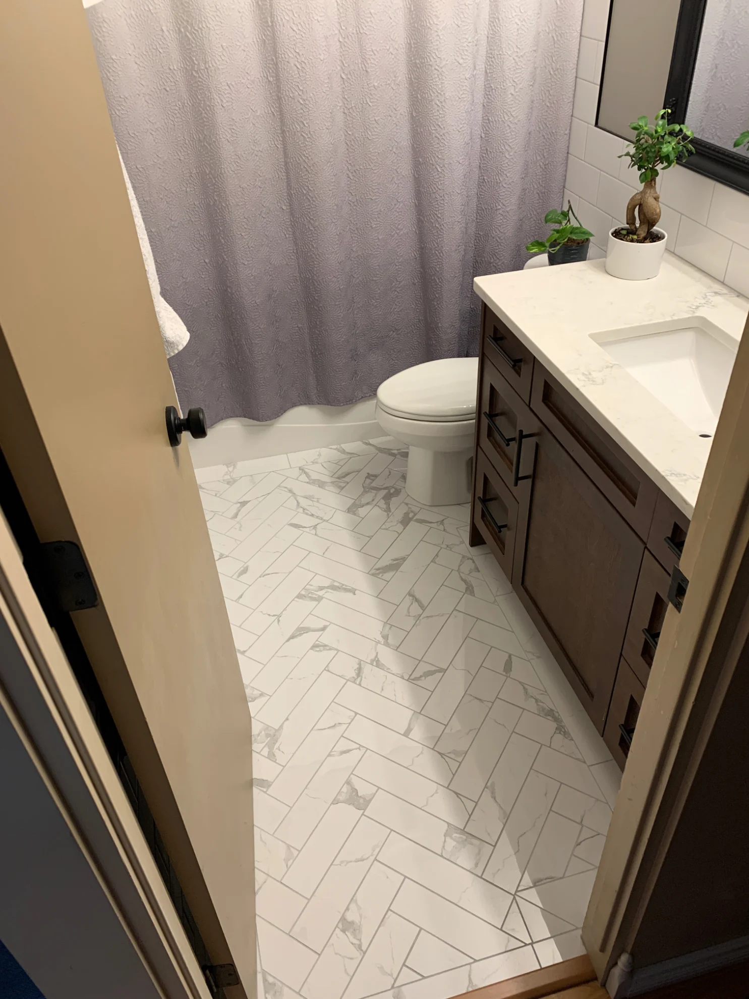 Modern Edmonton bathroom featuring a dark wood vanity with white countertops, an alcove, and intricate 3x10 herringbone marble immitation bathroom floor tiles.